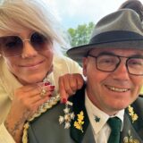 Eine Frau lehnt über die Schulter eines Schützen und präsentiert eine Kette und einen Orden.