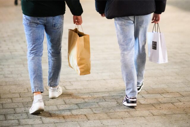 Zwei Passanten laufen am verkaufsoffenen Sonntag mit Einkaufstüten durch eine Innenstadt.