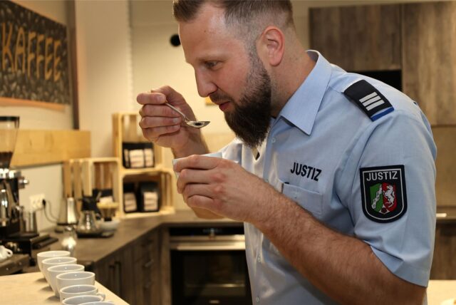 Betriebsleiter Daniel von Lonski probiert mit einem Löffel handgefilterten Kaffee aus der Rösterei der Justizvollzugsanstalt (JVA) Remscheid.