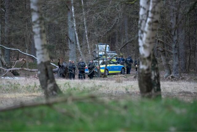 Polizeibeamte stehen mit mehreren Einsatzfahrzeugen nahe eines Tatortes in einem Wald.