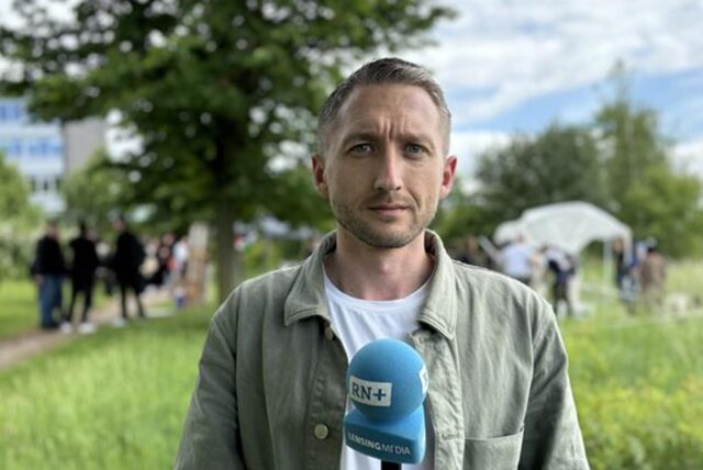RN-Reporter Philipp Pohl steht mit einem Mikrofon vor dem Protestcamp an der FH Dortmund.