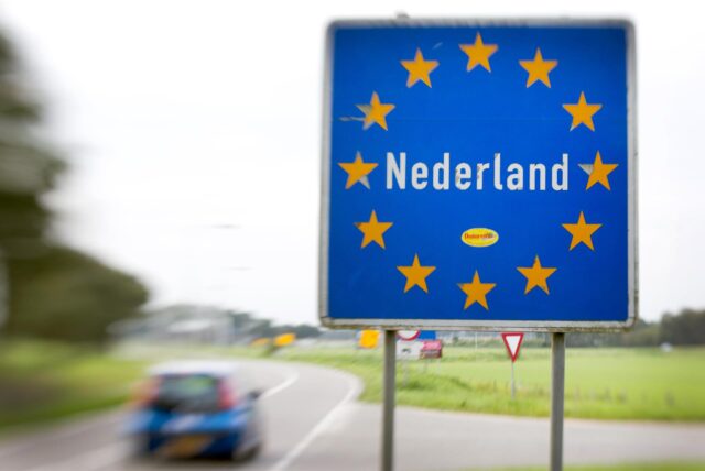 Ein Auto fährt an einem Schild mit der Aufschrift „Nederland“ vorbei, das an der Grenze zwischen den Niederlanden und Deutschland steht.