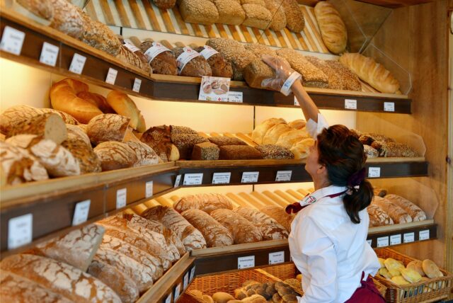 Eine Verkäuferin greift in einer Bäckerei in der Auslagen nach einem Brot.
