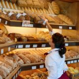 Eine Verkäuferin greift in einer Bäckerei in der Auslagen nach einem Brot.
