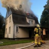 Zwei Feuerwehrleute stehen in voller Montur vor einem brennenden Wohnhaus in Bottrop.