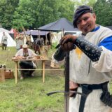 Ein Mann in historischer Kleidung posiert mit einem Schwert auf einem Mittelaltermarkt. Im Hintergrund sind Zelte und weitere Teilnehmer der Veranstaltung zu sehen. (Archiv)