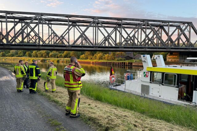 Eine Eisenbahnbrücke über einem Kanal. Im Vordergrund ein Schiff und Einsatzkräfte der Feuerwehr.