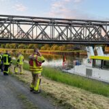 Eine Eisenbahnbrücke über einem Kanal. Im Vordergrund ein Schiff und Einsatzkräfte der Feuerwehr.