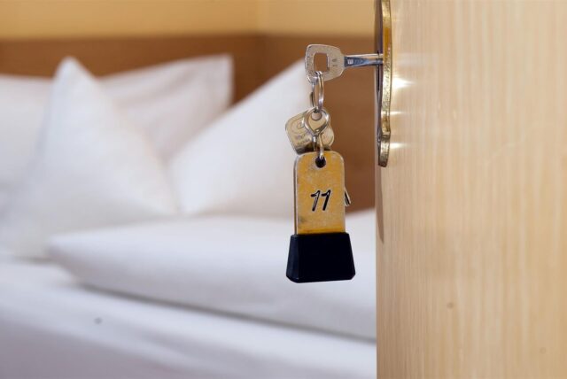Ein Zimmerschlüssel hängt in einem Gästehaus vor einem Bett im Türschloss.