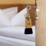 Ein Zimmerschlüssel hängt in einem Gästehaus vor einem Bett im Türschloss.