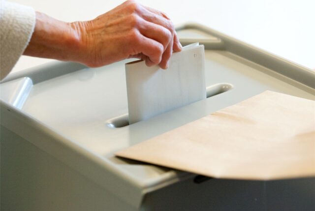 Frau steckt Wahlschein in eine Wahlurne