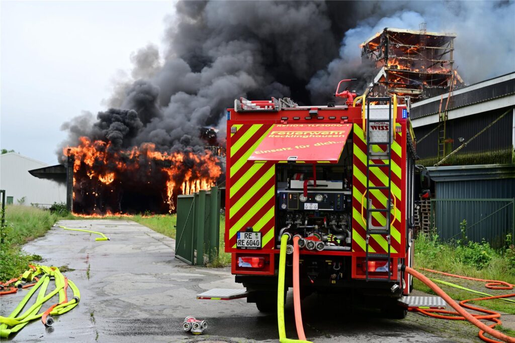 Ein Einsatzfahrzeug der Feuerwehr steht vor der brennenden Lagerhalle in Recklinghausen.