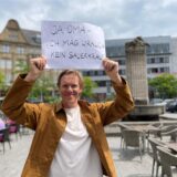 Simon Gosejohann steht auf dem Castroper Marktplatz vor dem Reiterbrunnen und hält einen Zettel mit der Aufschrift „Ja, Oma – ich mag wirklich kein Sauerkraut“ in die Luft.