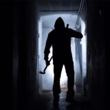 Ein Einbrecher hat im Dunkeln eine Brechstange in der Hand.