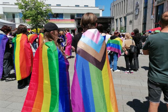 Zwei Jugendliche tragen eine Regenbogenflagge.