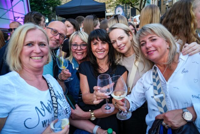 Frauen stoßen auf dem Abendmarkt in Recklinghausen mit einem Glas Wein an.