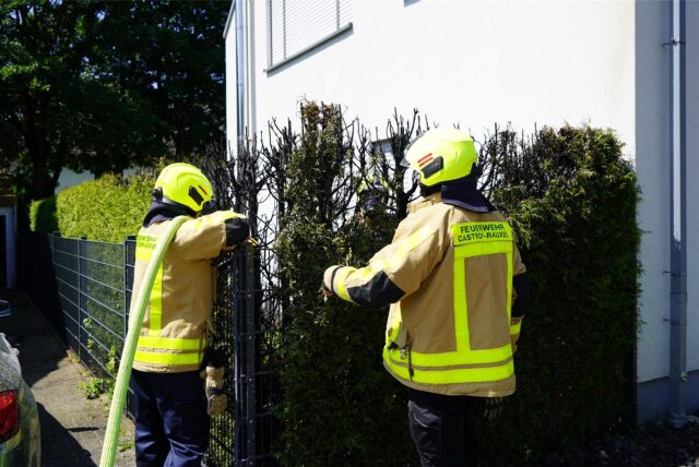 Feuerwehrleute beim Löschen vor iener verbrannten Hecke an ienem Wohnhaus im Hasenbkamp in Castrop-Rauxel.