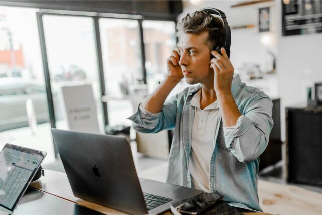 Ein junger Mann mit Headset sitzt in einem Büro vor seinem Laptop.