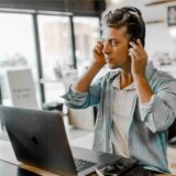 Ein junger Mann mit Headset sitzt in einem Büro vor seinem Laptop.