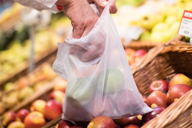 Ein Mann legt in einem Supermarkt einen Apfel in ein Mehrwegnetz.