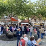 Viele Menschen stehen unter Bäumen und Schirmen.