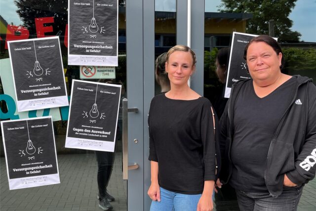 Zwei Frauen tragen schwarze Kleidung und stehen vor einer Kita-Tür.
