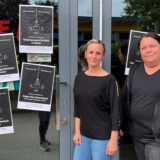 Zwei Frauen tragen schwarze Kleidung und stehen vor einer Kita-Tür.