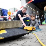 Tobias Bartels vom THW Herten kniet auf dem Boden und zeigt dem vierjährigen Lenny auf dem Hof vor dem Gerätehaus in Herten-Westerholt, wie das Hebekissen bedient wird.