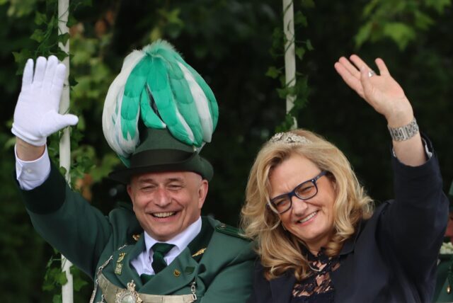 Ein Schützenkönig und eine Frau, die ein Diadem im Haar trägt, winken in die Kamera