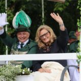 Ein Schützenkönig und eine Frau, die ein Diadem im Haar trägt, winken in die Kamera