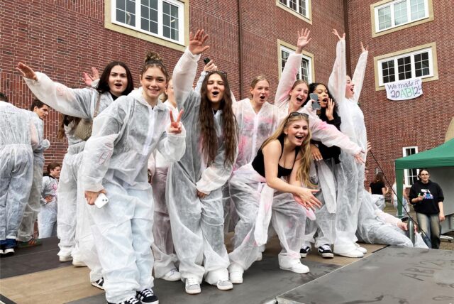 Eine Gruppe Jugendlicher steht in weißen Maleranzügen auf dem Schulhof des städtischen Gymnasiums und feiern ausgelassen.