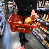 Eine Frau steht mit einem Einkaufskorb vor einem Lebensmittelregal im Rewe.