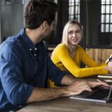 Zwei Männer und eine Frau diskutieren an einem Tisch mit Laptops über Business-Entscheidungen.