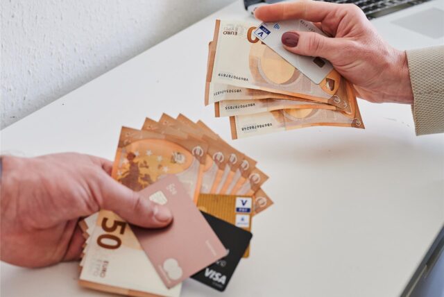 Männerhand und Frauenhand, jeweils mit einer Anzahl Geldscheine und Kreditkarten.