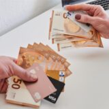 Männerhand und Frauenhand, jeweils mit einer Anzahl Geldscheine und Kreditkarten.