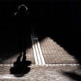 Eine Frau geht über eine Straße, die halb im Schatten liegt.