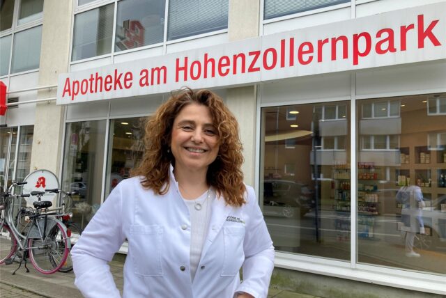 Mel Ermeidi hat mit 52 Jahren ihre Ausbildung zur Pharmazeutisch Kaufmännischen Assistentin bestanden. Hier steht sie im weißen Kittel vor der Apotheke am Hohenzollernpark in Recklinghausen, wo sie zuvor schon jahrelang als Aushilfe gearbeitet hatte.