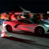 Ein Sportwagen fährt in der Dunkelheit, im Hintergrund ist verschwommen das Publikum des Autorennens zu sehen.