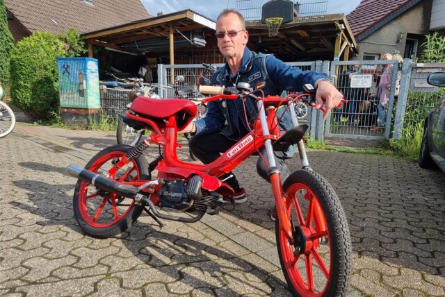 Ein Mann kniet hinter einem Mofa.
