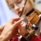 Eine Musiklehrerin korrigiert die Hand einer Schülerin beim Geigenspiel.