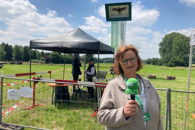 Eine Frau steht mit Mikrofon auf der Vogelwiese