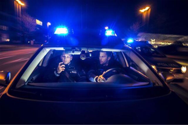 Zwei Polizisten in einem fahrenden Streifenwagen mit Blaulicht