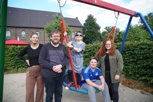 Fünf Menschen stehen auf einem Spielplatz und lächeln in die Kamera.