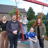 Fünf Menschen stehen auf einem Spielplatz und lächeln in die Kamera.