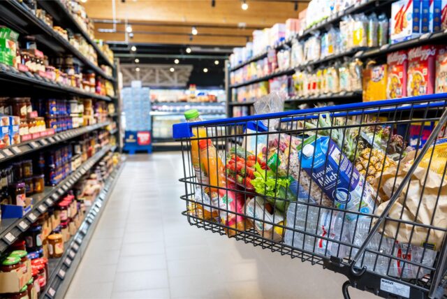 Ein gefüllter Einkaufswagen steht im Gang im Supermarkt.