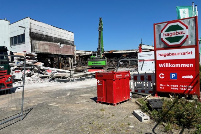 Überreste des Hagebaumarkts in Castrop-Rauxel, an dem ein grüner Bagger den Schrott aufsammelt.