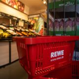 Ein Einkaufskorb mit dem Logo der Supermarktkette Rewe steht vor einer Obstauslage.