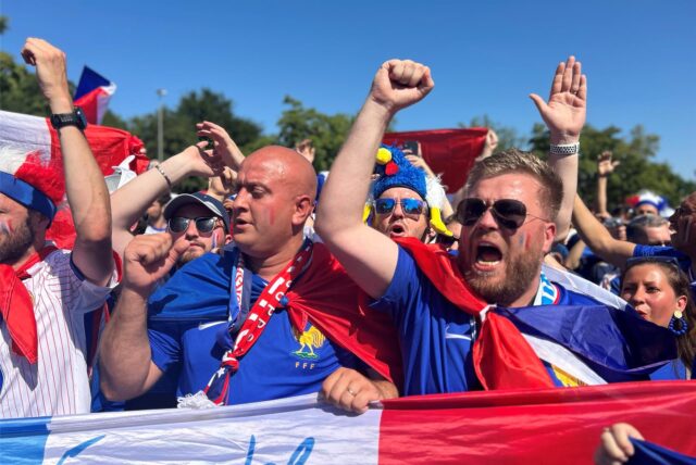 Französische Fußball-Fans rufen Fangesänge und halten die französische Flagge vor sich.