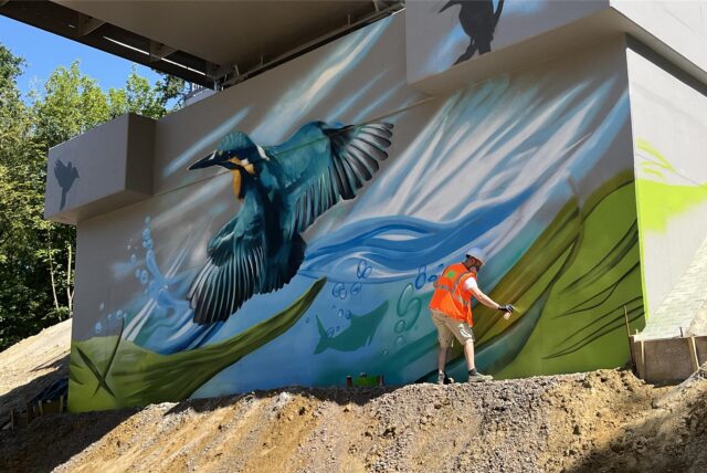Max Packheiser sprüht den Background für den Eisvogel am Fundament der neuen Stahlbrücke am Vater-unser-Weg.