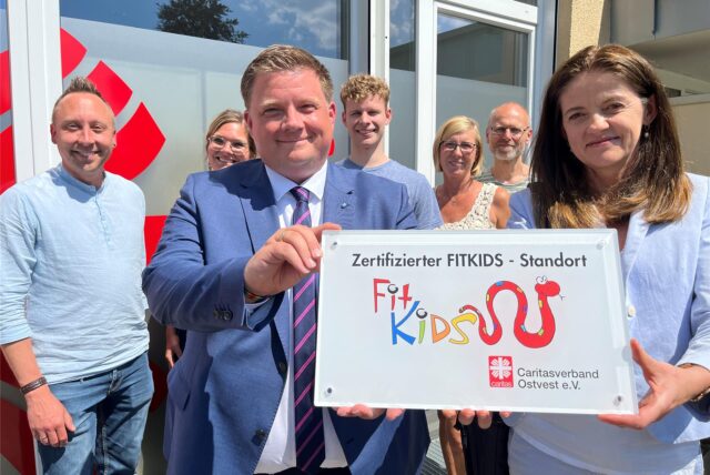 Caritas-Mitarbeiter und Bürgermeister zeigen „Fitkids“-Siegel.